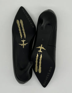 Classic black pump with a golden airplane image stamped against black outsole.
